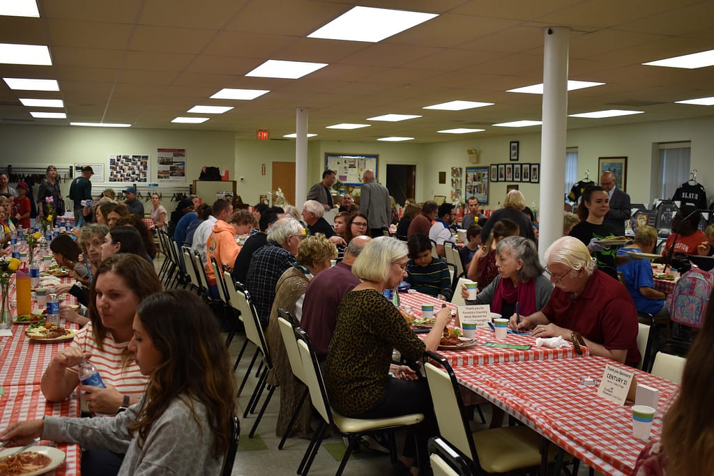 Spaghetti Dinner attendees sit at tables eating their dinners and socializing with one another